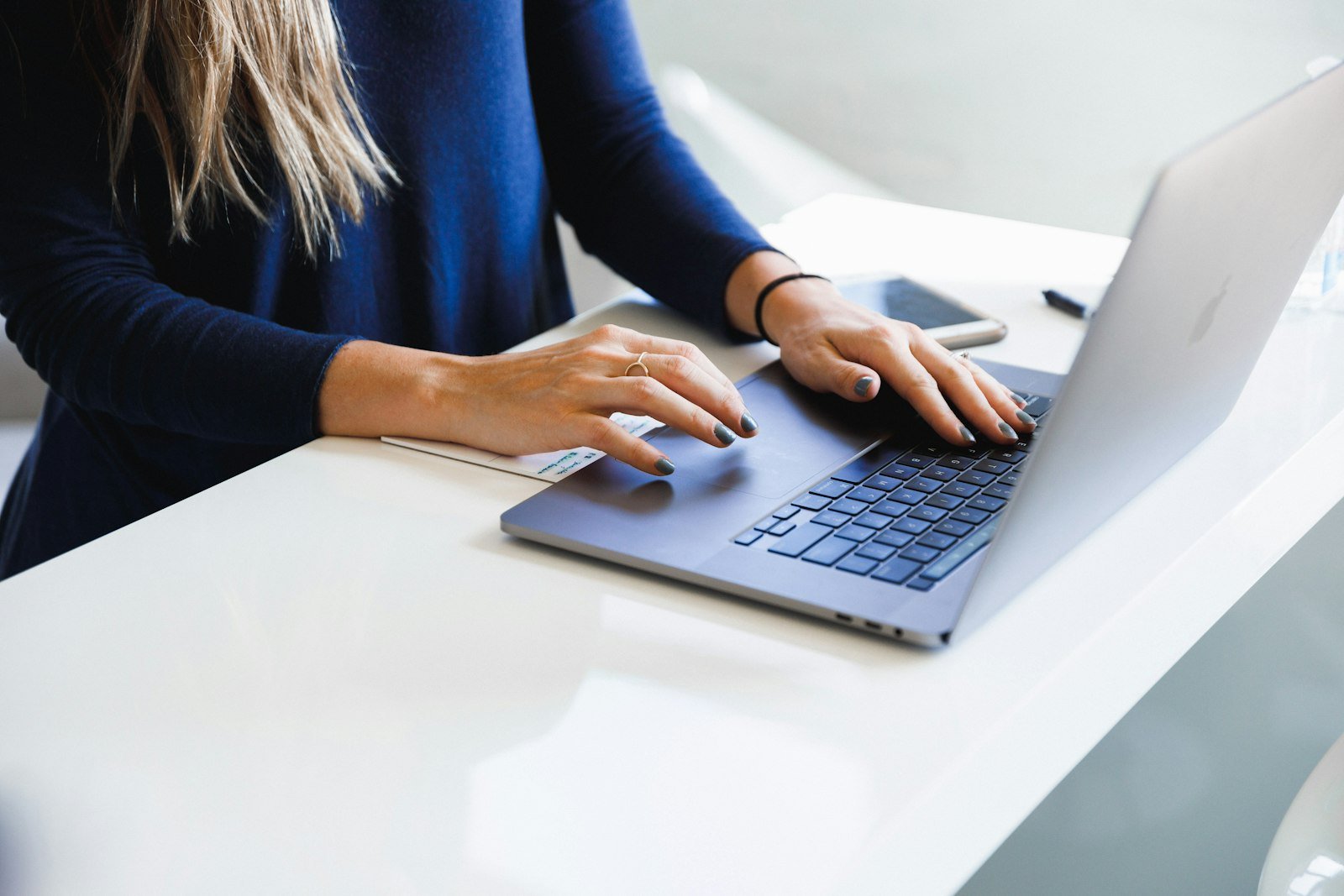 Mains sur le clavier d’un ordinateur portable posé sur un bureau blanc